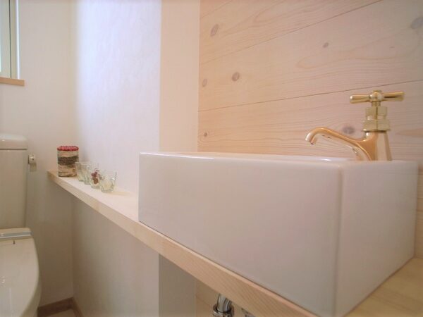 シンプルだけど、ゴールドの水栓がかわいいトイレ手洗い。小さめサイズ。カウンターはトイレの奥まで伸ばして、ちょっとした飾り棚に！手洗器の前の壁には板張り